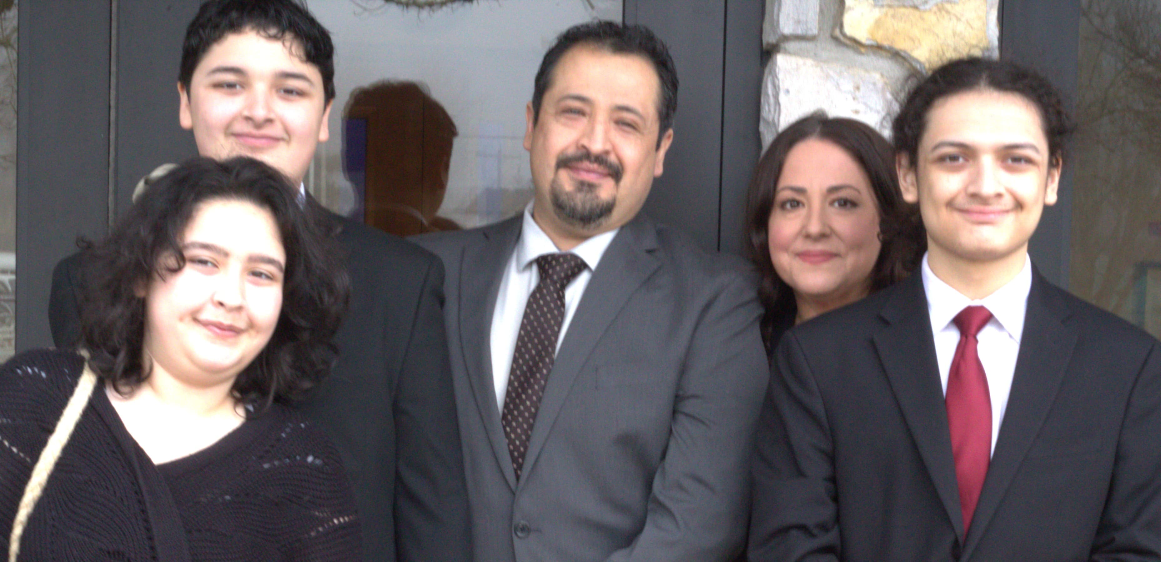 A smiling family of five in formal suits and attire posing for a group portrait.